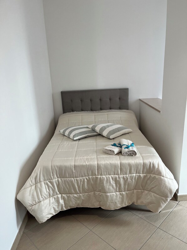 A neatly made bed with a grey headboard, two striped pillows, and a folded towel with a blue ribbon.