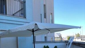 Eine Terrasse im Freien mit einem weißen Sonnenschirm, weißen Stühlen, einem kleinen Tisch und einem Topfpflanzen.