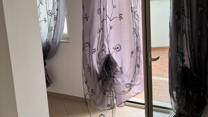 Ein Zimmer mit einer Schiebeglasdoor, Blick ins Freie und zarten Vorhängen mit Blumenmuster.