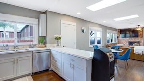 Een moderne keuken met een centraal eiland, een eethoek met blauwe stoelen, en een woonkamer met een open haard.