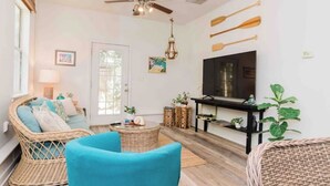 A living room with wicker furniture, a ceiling fan, a TV, and a door. - Cottage on River (Jacksonville)