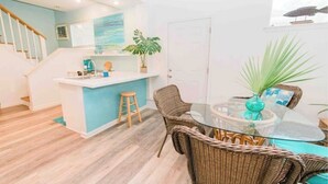 A modern kitchen with a central island, a dining area with wicker chairs, and a staircase leading to an upper level. - Cottage on River (Jacksonville)