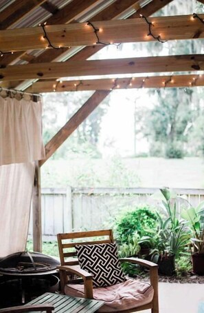 A covered outdoor seating area with wooden furniture, string lights, and potted plants. - Cottage on River (Jacksonville)
