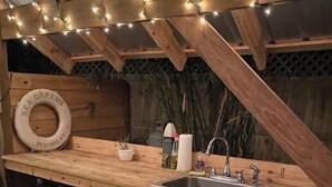 A rustic wooden kitchen with a sink, a small refrigerator, and string lights. - Cottage on River (Jacksonville)