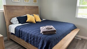 Una camera da letto con una struttura del letto in legno, una coperta trapuntata blu, due cuscini e un asciugamano piegato sul letto.