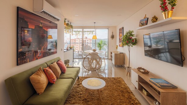 A modern living room with a green sofa, a round coffee table, and a flat-screen TV mounted on the wall. - Moderno Apartamento con diseño caribe (Cartagena)