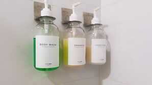 Three bottles of body wash, shampoo, and conditioner on a white tiled wall. - Moderno Apartamento con diseño caribe (Cartagena)