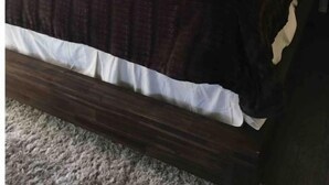 Una cama bien hecha con un cabecero oscuro, un almohadón blanco y una manta oscura.
