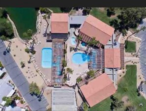 Vista aérea de un complejo turístico con varias piscinas, una zona de playa y un edificio grande con techo rojo.