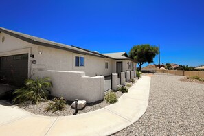 Une maison d’habitation avec un garage, un petit jardin agrémenté d’un palmier, et un ciel d’un bleu éclatant.