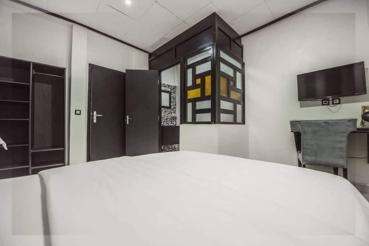 Ett modernt hotellrum med en stor säng, en garderob, en tv som är monterad på väggen och ett litet skrivbord med en stol.