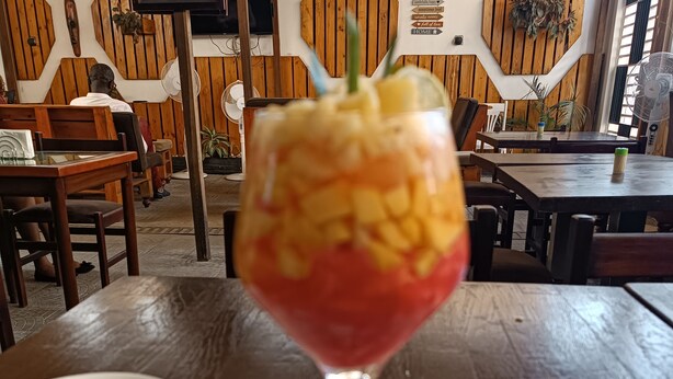 A glass of red drink with a straw on a table in a restaurant with wooden walls and furniture. - Villa des roses (Douala)