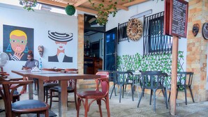An outdoor café with wooden tables and chairs, a mural on the wall, and a menu board. - Villa des roses (Douala)