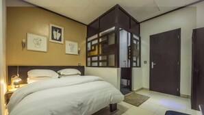 A hotel room with a large bed, a wardrobe, a desk, and a door. - Villa des roses (Douala)