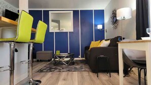 Een kleine leefruimte met een bank, twee stoelen, een tafeltje en een spiegel.
