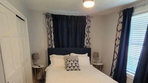 Een slaapkamer met een bed, een plafondventilator, een kamerbreed tapijt met een patroon en een raam met gordijnen.