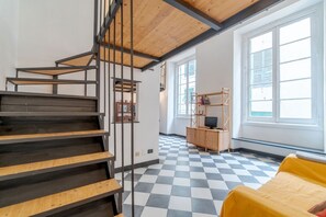 Una escalera con escalones de madera y barandas de metal, un suelo a cuadros, una cama amarilla y un armario de madera con un televisor.
