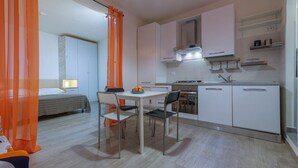 Cocina compacta con armarios blancos, estufa y lavabo. Hay una zona de comedor con una mesa y sillas.