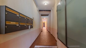 Un pasillo con una fila de taquillas metálicas, suelo de baldosas y una puerta de cristal a la derecha.