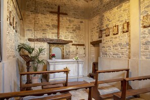 A church interior with stone walls, wooden pews, a central altar, and religious statues.
