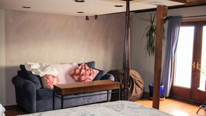 A room with a bed, a sofa, a wooden coffee table, and a potted plant.