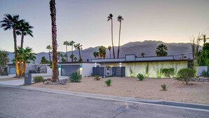 Una casa moderna con garage, circondata da palme e con una montagna sullo sfondo.