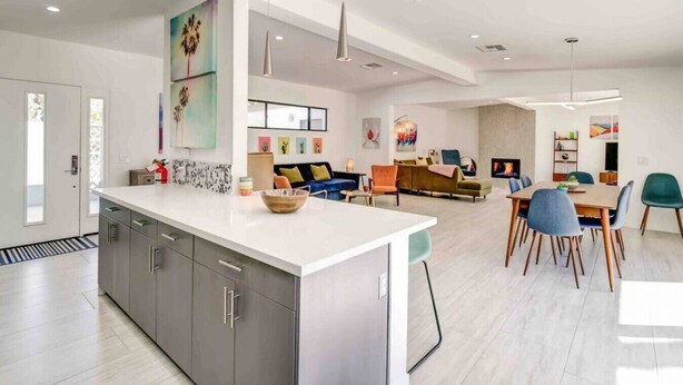 Una cucina moderna con una grande isola, una zona pranzo con tavolo e sedie in legno, e un soggiorno con divano e televisione.