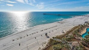 Una playa con un muelle que se adentra en el mar, una piscina y una fila de sillas.