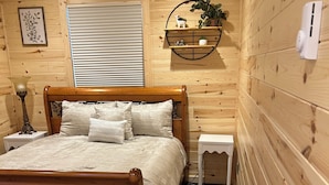Um quarto rústico em estilo cabana, com uma cama, mesas de cabeceira, um abajur e uma prateleira na parede com plantas.