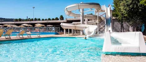 Une piscine avec un toboggan, des chaises longues et des parasols.