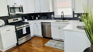 A modern kitchen with white cabinets, stainless steel appliances, and a wooden floor.