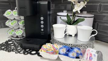 A coffee maker, coffee pods, a plant, and two white cups on a countertop.