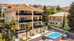 Ein mehrstöckiges Gebäude mit Pool auf dem Dach, Balkonen und umgebender Bepflanzung.