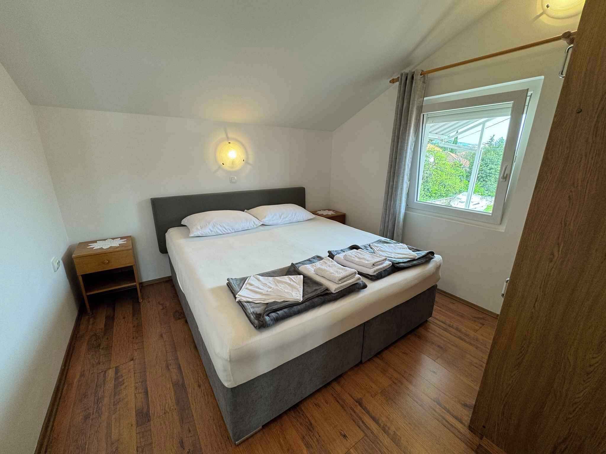 Un dormitorio con cama, mesitas de noche, una lámpara de pared y una ventana con cortinas.
