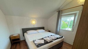 A bedroom with a bed, bedside tables, a wall-mounted light, and a window with curtains. - Holiday apartment with balcony and sea view (Crikvenica)