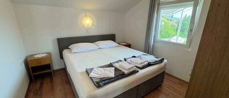 Un dormitorio con cama, mesitas de noche, una lámpara de pared y una ventana con cortinas.