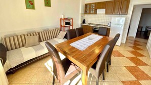 A dining area with a wooden table, four chairs, a sofa with striped cushions, and a kitchen in the background. - Holiday apartment with balcony and sea view (Crikvenica)
