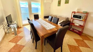 A dining area with a wooden table, black chairs, and a view of the sea through large windows. - Holiday apartment with balcony and sea view (Crikvenica)