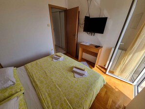 Un dormitorio con una cama, un escritorio, un televisor y una puerta corrediza de vidrio.