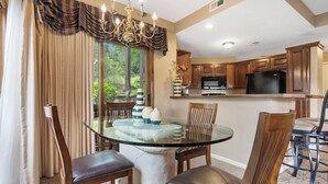 A dining area with a glass table surrounded by wooden chairs, a chandelier, and a view of the outdoors through large windows. - StoneBridge Village Villa - Located Minutes from Silver Dollar City (Reeds Spring)
