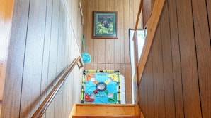 Un escalier en bois, doté d’une rampe, mène à une pièce aux murs en bois et ornée d’un tableau encadré.