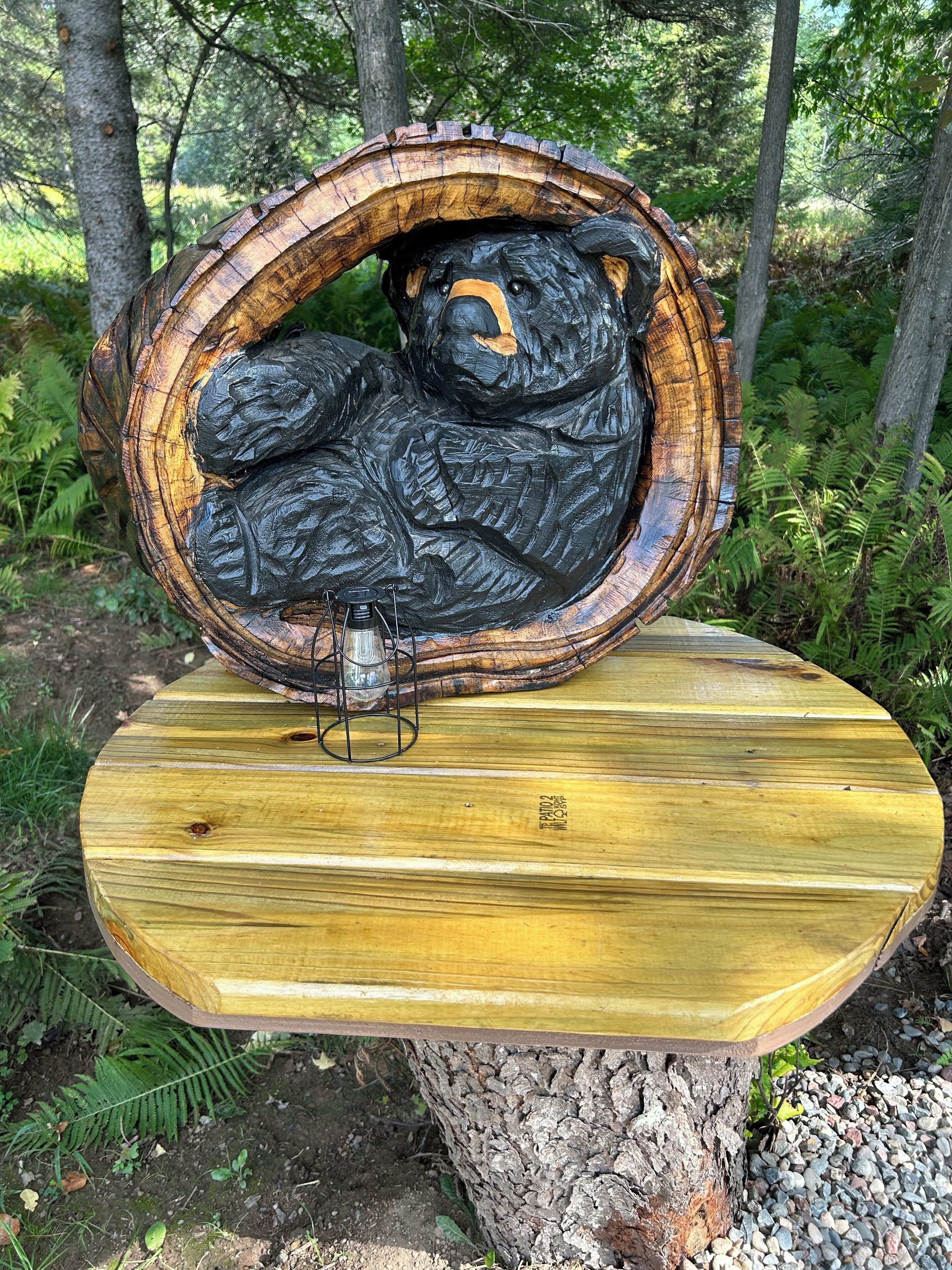 A wooden sculpture of a bear in a tree hollow, placed on a wooden table outdoors.