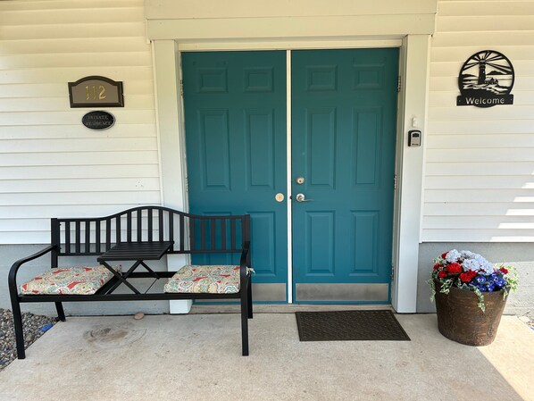 Une porte à deux battants de couleur turquoise, avec un paillasson et un banc agrémenté de coussins à motifs devant.