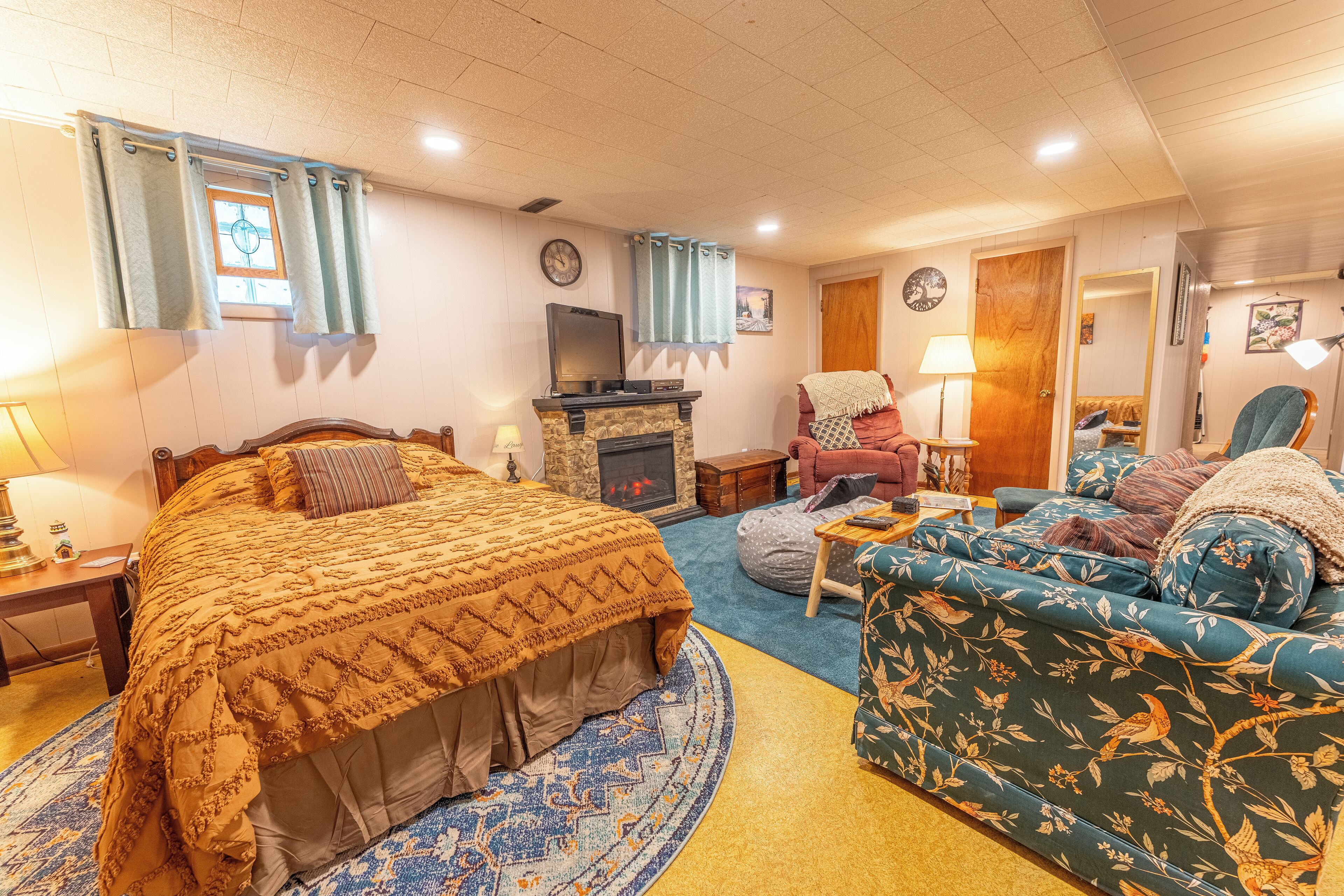 A cozy room with a bed, a sofa, a fireplace, and a clock on the wall.
