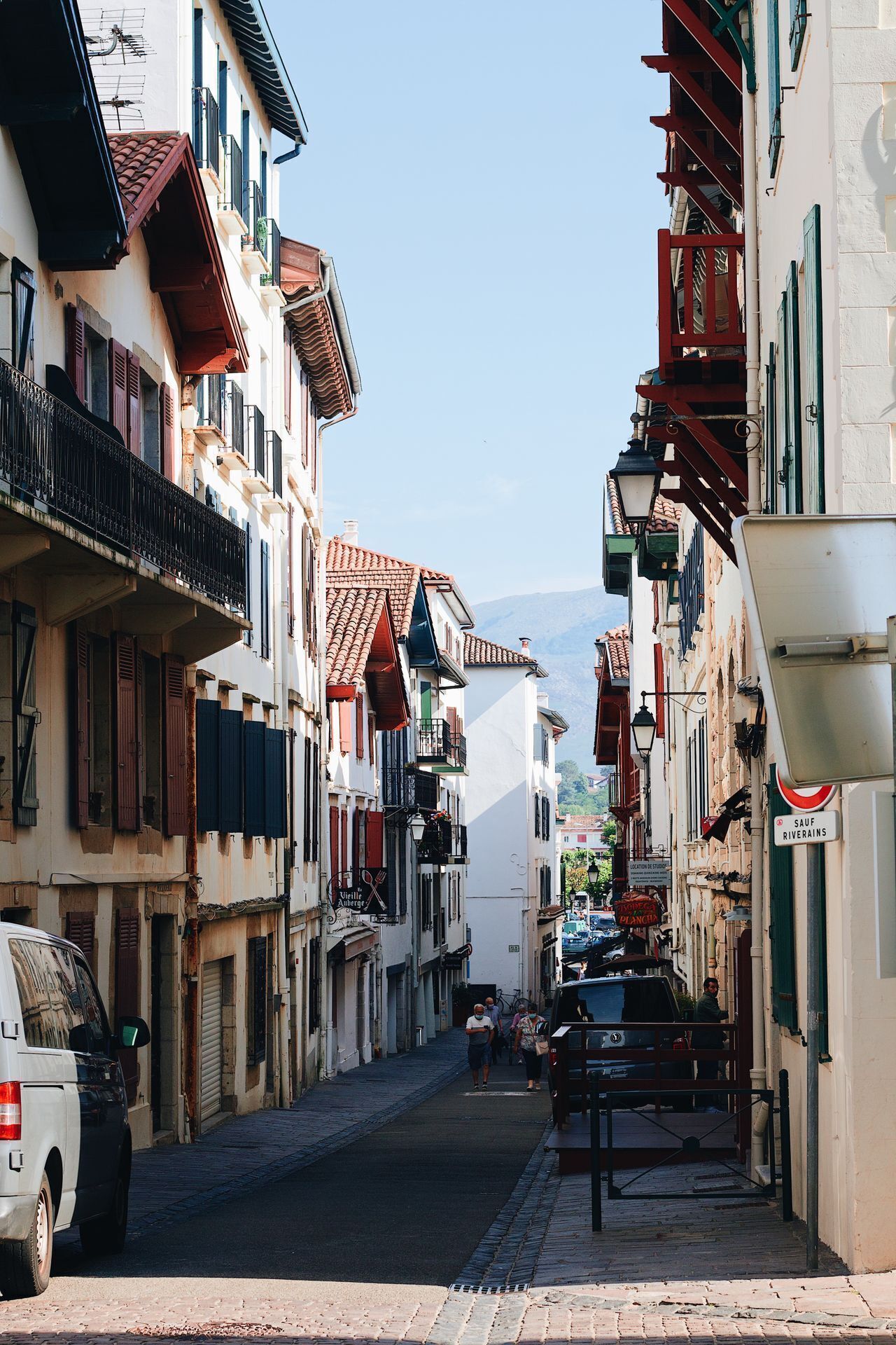 Uma rua estreita ladeada por edifícios, um carro estacionado e uma van.