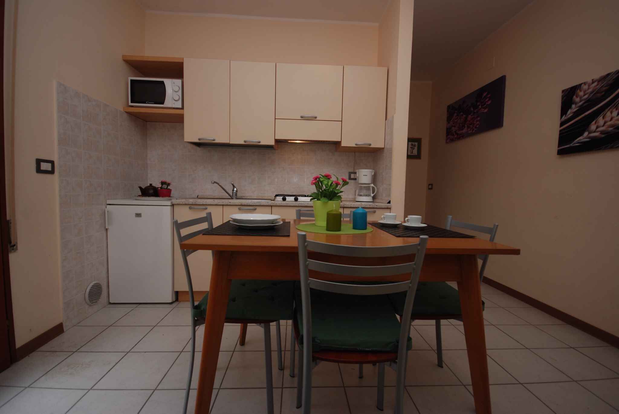 A compact kitchen with a microwave, stove, and sink. There is a dining table with chairs and a small refrigerator.