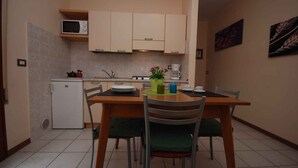 Une cuisine compacte équipée d’un four à micro-ondes, d’une cuisinière et d’un évier. On y trouve une table à manger avec des chaises et un petit réfrigérateur.