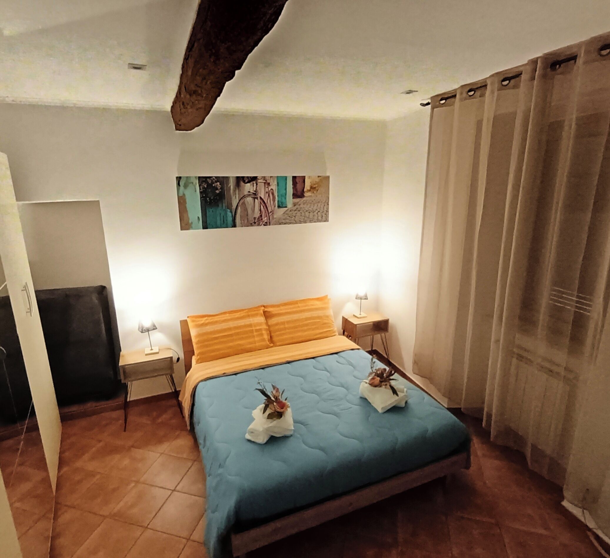 Une chambre à coucher avec un lit, deux tables de chevet, un tableau accroché au mur et une fenêtre avec des rideaux.