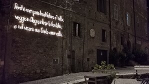 Un espace extérieur comprenant un bâtiment en pierre, une table avec des chaises et un panneau lumineux avec du texte.