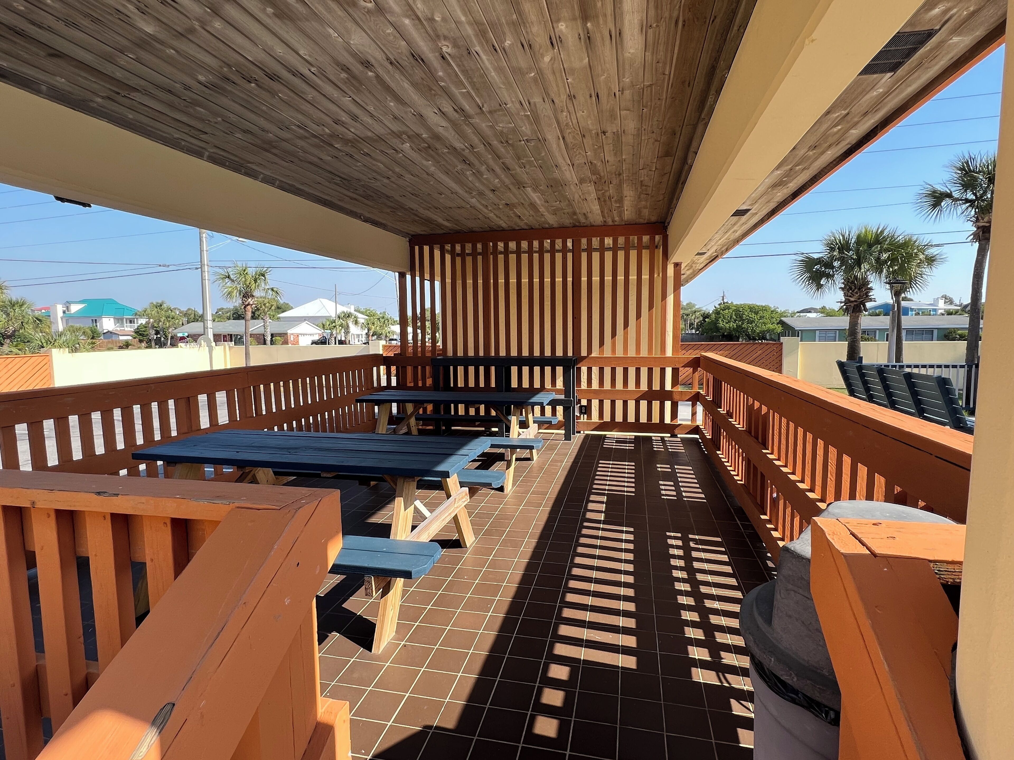 A covered outdoor patio with wooden benches and tables, a tiled floor, and a view of the neighborhood.